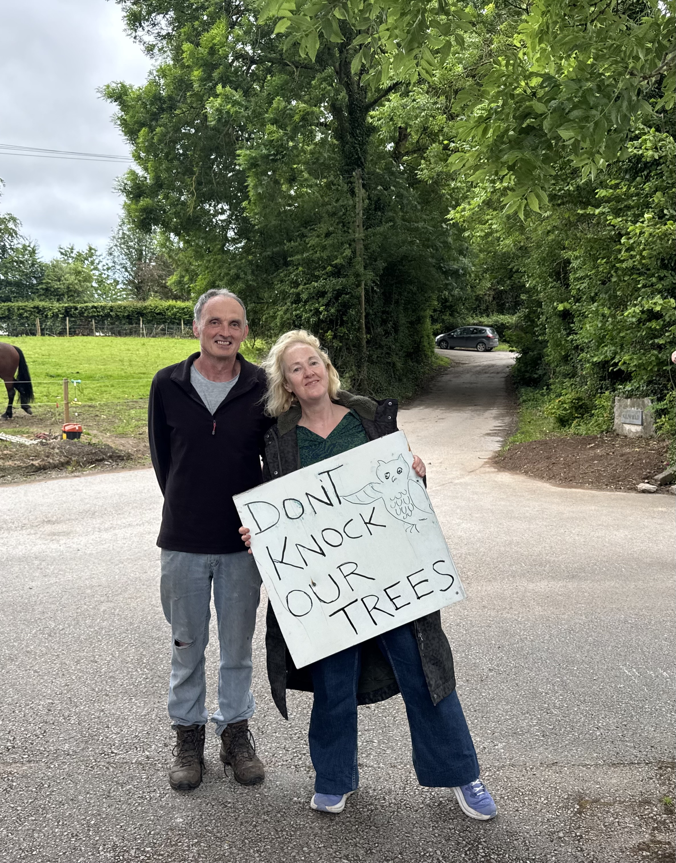 Couple holding Don't Knock Our Trees sign on the lane